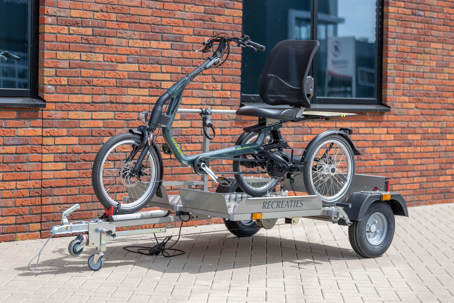 Scootwagen trailer met een driewielfiets erop, voor een bakstenen muur