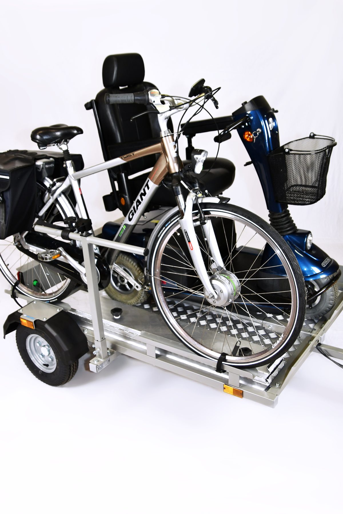 Trailer met een scootmobiel en twee fietsen erop, voor een witte achtergrond